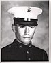 Head of a young white man wearing a white peaked cap with black visor and a dark military jacket.