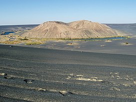A white hill within a black depression, with lakes and vegetation at its foot and desert elsewhere