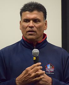 Anthony Munoz in a Pro Football Hall of Fame sweater speaking into a microphone.