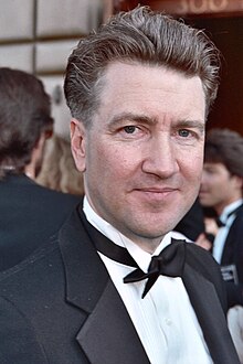 A man in a tuxedo looks directly at the camera, slightly smiling