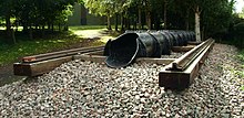 Exterior in woodland. a short section of railway line on wooden sleepers with a cast iron pipe of approximately one foot diameter, running inline with the rails