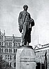 B&w photo of a statue, with multi-storey buildings in the background
