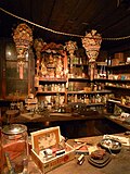 Interior photograph of the Kam Wah Chung Company building showing a general store area, dimly lit, with many products on counters, tables, shelves, and hanging from the wood plank ceiling. Many products are conspicuously Chinese in style, and all furniture and building elements are wooden.