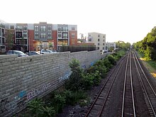 A below-grade railroad corridor, with a retaining wall and housing development at left