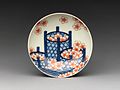 A small dish with pink cherry blossoms in blue bamboo baskets. White porcelain decorated in colored enamels.