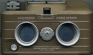 A view master camera from the front, showing the twin lenses and brown color of the body. The viewfinder is visible above the lenses, and a small dial to select between "A" and "B" settings is visible between the lenses.