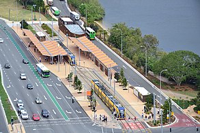 An aerial view of the station and bus interchange. The station is a single track station with platforms on either side. There are street-level open-air structures featuring passenger canopies on both platforms. Bus stops and roads are visible either side of the station.