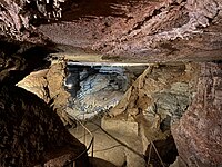 Entrance to the "Council Room" part of the cave's interior. Their is a paved walkway with handrails leading down to the room. The walls and ceiling are formed with pink and tan limestone rock