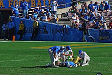 Photo of Jones at UCLA laying on a field surrounding by team trainers