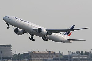 Front quarter view of the first 777 built in flight wearing Cathay Pacific livery and with flaps partially extended and landing gear retracted.