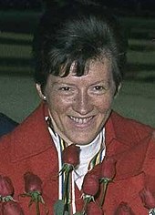 A smiling woman, wearing red, holding flowers.