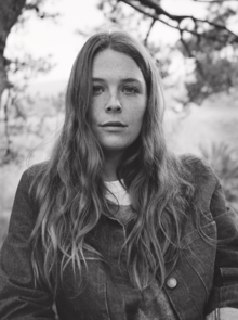 Grayscale photo of a woman in nature with long hair and wearing layers