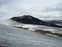 A black cone-shaped mountain rising over glacial ice in the foreground.