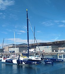 Trimaran bleu et blanc vu de trois quarts avant, amarré au ponton.