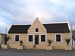 T-shaped dwelling with adjacent attached building. Type of site: House Current use: Commercial. Originally one of the gabled houses erected near the Dutch Reformed Church. Possibly the first erf in Calvinia to be measured.