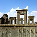 Ruins of buildings and a frieze depicting humans carrying staffs or lances.