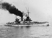 A large gray battleship moves slowly through calm seas