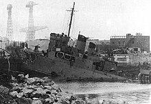 ship at 45-degree angle showing damage caused by German gunfire and impact with the dock