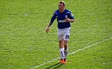 A footballer wearing a blue shirt and white shorts