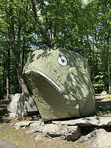 A large boulder, painted light green, with eyes and lip drawn on the face to resemble a frog