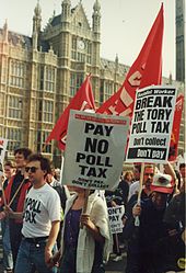 Protesters marching in front of the Palace of Westminster carrying red banners and placards with anti-poll tax slogans: "Don't Pay – Don't Collect"