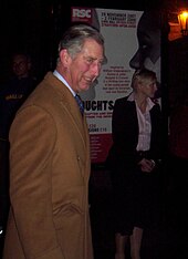 Charles in a brown coat attending a performance of Henry V in Stratford-upon-Avon