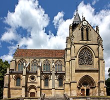 Notre-Dame de l'Assomption à Taverny, vue latérale avec à droite, le porche principal (porte du roi Jean), séparé du clocher par une rosace en vitrail ; à gauche, série de quatre vitraux en ogive, avec remplages de pierre très travaillés. Au-dessous, bas-côtés avec série de trois vitraux en ogive. Sous le second emplacement à partir de la gauche, porte secondaire d'entrée, surmontée d'un petit vitrail en œil-de-bœuf. On distingue très nettement les contreforts.