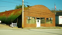 A brick facade in front of a curved metal building with rust and green paint