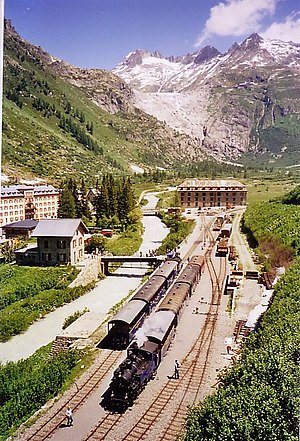 Two steam locomotive-pulled trains in a railway yard nestled in a valley