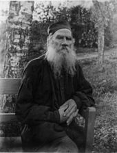 Photo noir et blanc d'un vieillard à grande barbe blanche, assis mains croisées sur un banc dans un jardin.