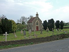 Small stone building with gravestones in the foreground.