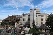 Photographie en couleur d'une station ferroviaire au premier plan et de bâtiments au second plan.