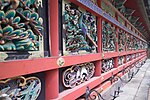 Wooden wall with red beams and colored carvings of plants, peacocks and other birds.