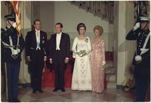 Photographie couleur de deux couples en tenue d'apparat, entourés de deux soldats.