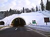 Tunnel portal, variable traffic signs indicating traffic flow direction and speed limit enforced are visible at the tunnel entrance and to the side of the road