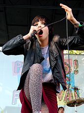 Alice Glass pictured from below, singing into a microphone while crouching down.