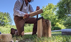 photo d'un homme appuyé sur un genou qui utilise un départoir en le frappant avec maillet pour fendre un billot.