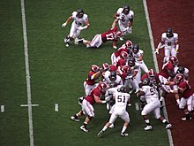 American football players in middle of a running play near the endzone.