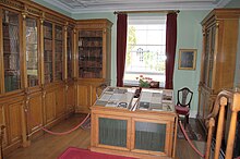 Photograph of a laboratory, with glass-encased, wooden bookcases on two walls and a window on the third. There is a display case in the middle of the room.