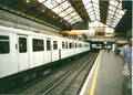 A picture of Earl's Court tube station in the year 1999. Note the crowded staircase behind the train.