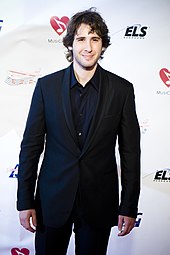 A young man with collar-length dark-hair wearing a dark suit and dark shirt