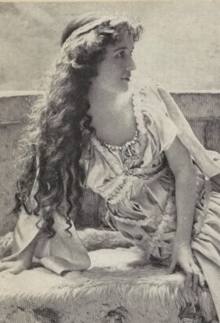 A young white woman with long wavy hair, reclining on a bench