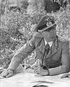 A man wearing a military uniform, peaked cap, and an Iron Cross displayed at the front of his uniform collar.