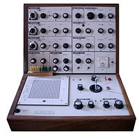 Machine électronique avec un tour en bois. L'espace principal est gris avec plusieurs boutons et variateurs noirs.