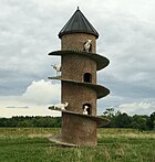 Photograph of a round brick tower with a ramp spiralling from the ground to the roof, with several goats standing on the ramp