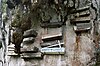 A wall of rock with several wooden coffins hanging on it.