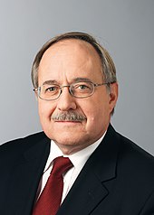 Photographie d'un homme portant une moustache et des lunettes.