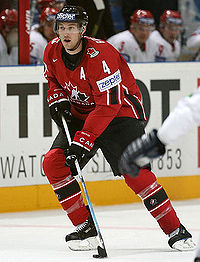 Hockey player in red uniform. He guides the puck across the ice with his stick.