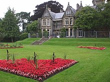 Photograph of garden and lawn in front of a sandstone mansion