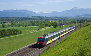 Red, blue, and white electric multiple unit on double track running through green fields